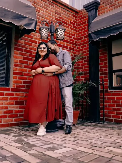 A sweet and casual moment during a pre-wedding shoot against a rustic brick wall, showing the couple in a relaxed and affectionate embrace.