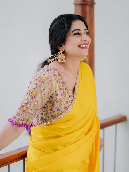 A close-up of a unique color combination: a bright yellow saree paired with a multi-color embroidered blouse with purple tassels.