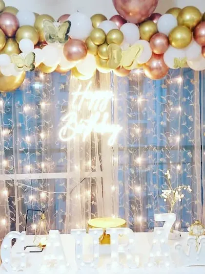 A glamorous home setup for a 7th birthday party. The decor features a gold and white balloon garland, a neon sign, and foil crown balloons for a royal touch.