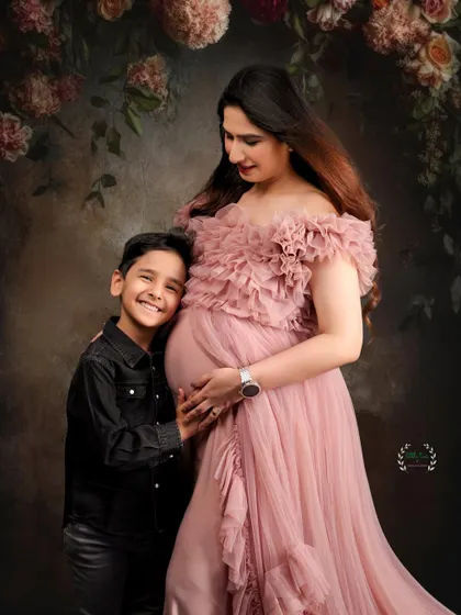 Welcoming a new sibling is a special time. This portrait captures a proud big brother with his hand on his mother's baby bump, set against a romantic floral arch.