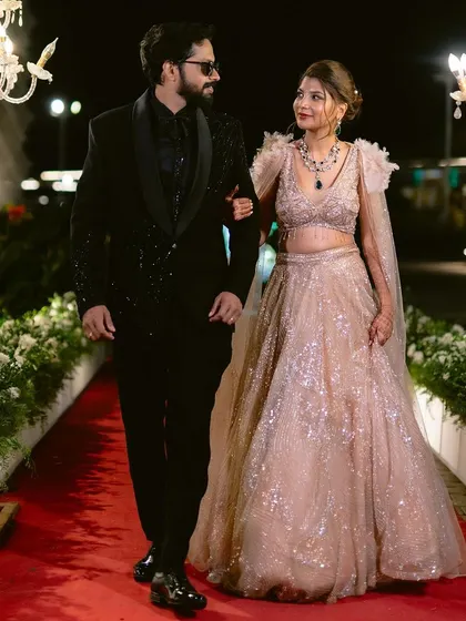 The couple's reception entrance, walking down a formal red carpet. The elegant chandeliers and floral borders add to the sense of occasion and luxury.