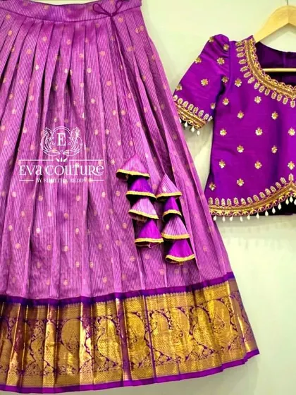 A royal purple pattu pavadai set. The pleated silk skirt has a wide gold zari border, and the matching blouse is adorned with delicate pearl and gold butti embroidery.