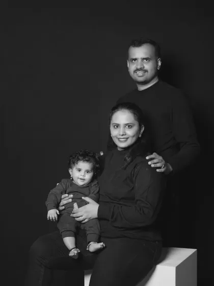 A formal black and white studio portrait of a family of three, looking poised and happy.