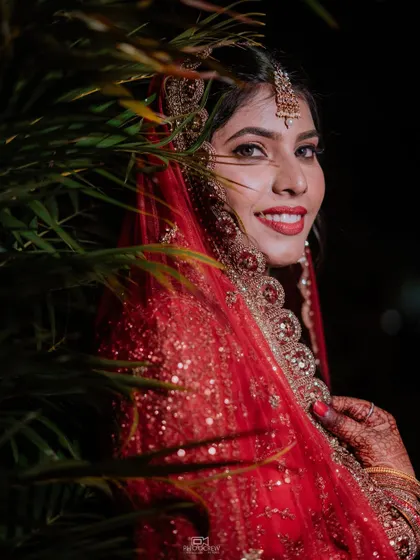 A candid, smiling portrait of the bride, partially framed by greenery, creating a natural and soft look.