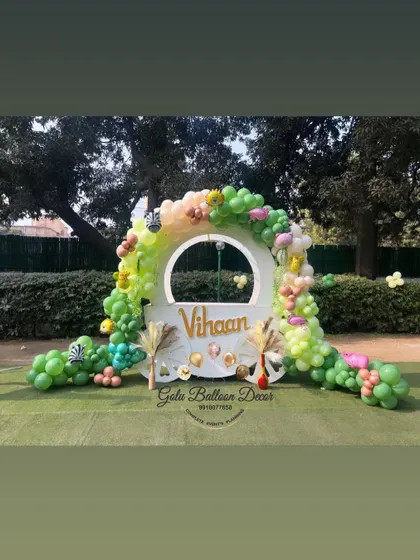 A beautiful circular photo booth for a jungle-themed party, personalized with the name "Vihaan" and surrounded by a green balloon arch.