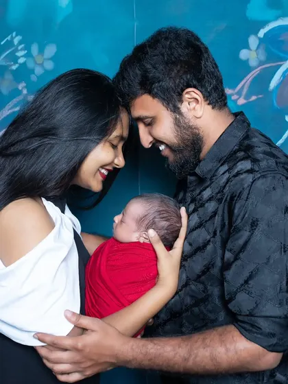 A happy couple with their newborn, their smiles lighting up the frame. The red wrap on the baby adds a beautiful pop of color.