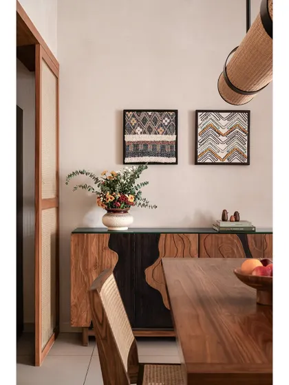 The dining console in 'Kayu' is a perfect example of layering. The unique wood grain and sculptural form add visual interest to the space, complementing the natural textures of the dining set and wall art.