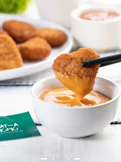 An action shot of a nugget being dipped in sauce is engaging and dynamic. It focuses on the experience of eating, making the food feel more interactive and desirable.