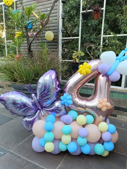 This close-up shows a custom arrangement for a fourth birthday, combining a large rose gold number '4' foil balloon with a whimsical purple butterfly and a pastel balloon cluster. It's a perfect centerpiece or photo prop for the celebration.