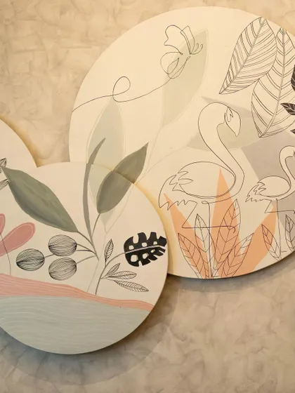 A close-up of the hand-painted circular canvases for Cafe Tesu, featuring a mix of line art and painted botanicals and flamingos.