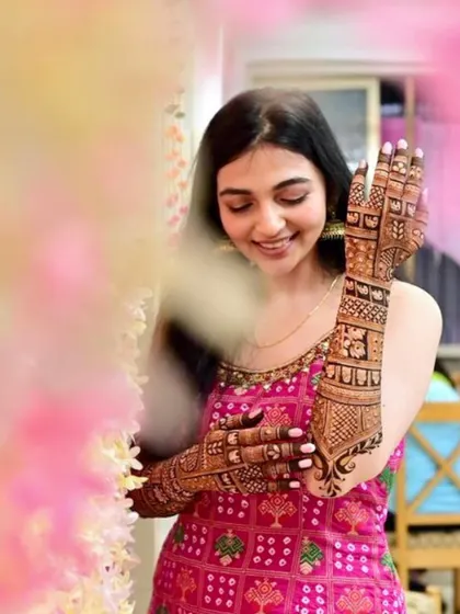 A happy bride admiring her intricate mehendi, which features family portraits and traditional motifs.