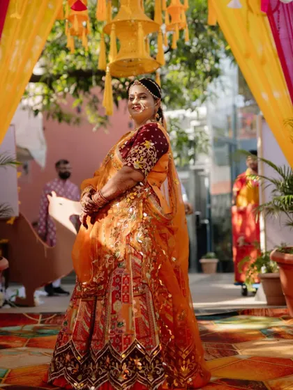 Dressed for a wedding function, our client looks stunning in a custom orange lehenga with intricate traditional motifs and a heavily embroidered maroon blouse.