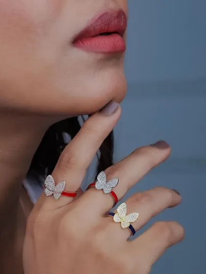 A detailed macro shot of a model wearing three butterfly rings with colorful bands. This image highlights the fine craftsmanship and vibrant design of the product for an e-commerce listing.
