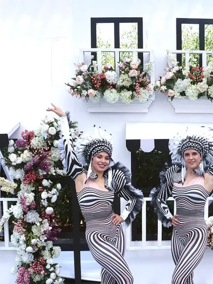 Performers in striking black and white costumes pose against a European-inspired facade adorned with flowers, blending art and entertainment.