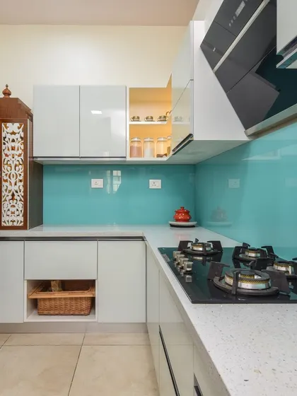 This angle shows the L-shaped layout of the kitchen, which also incorporates a small, beautifully carved wooden pooja cabinet on the countertop, blending spirituality with modern design.