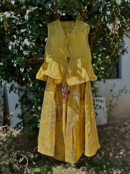 This mustard yellow lehenga set features a stylish peplum top with ruffles and a printed skirt with delicate bird motifs. It's a modern and chic option for a Mehendi or Haldi function.