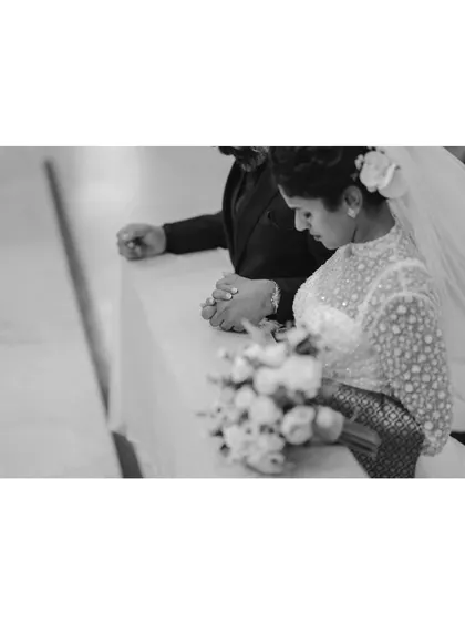 A black and white shot of the couple kneeling in prayer during their wedding ceremony. This quiet, reverent moment highlights the importance of faith in their journey together.
