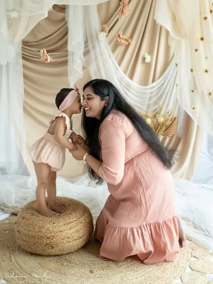"Amma." A daughter whispers a secret to her mother, a beautiful and intimate moment captured during their photoshoot. The soft pink tones add to the tenderness.