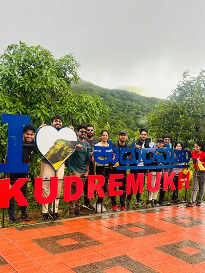 Another group at the "I Love Kudremukha" sign, holding a custom heart with a view of the peak.