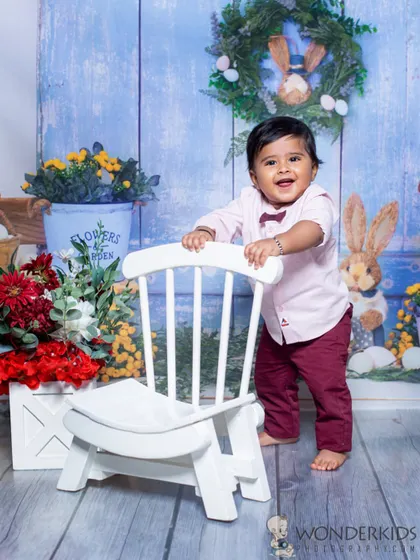 A happy baby boy in a spring garden setup. The bright flowers, bunny props, and his joyful smile make this a very cheerful and lively portrait.