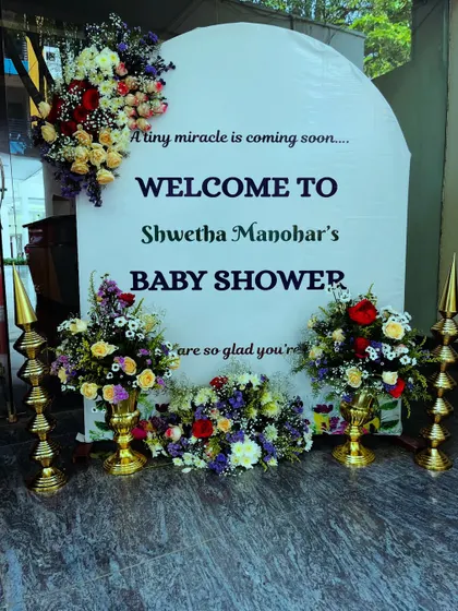 An elegant welcome sign for a baby shower. The board is decorated with an arch of fresh flowers, creating a beautiful and inviting entrance for guests.