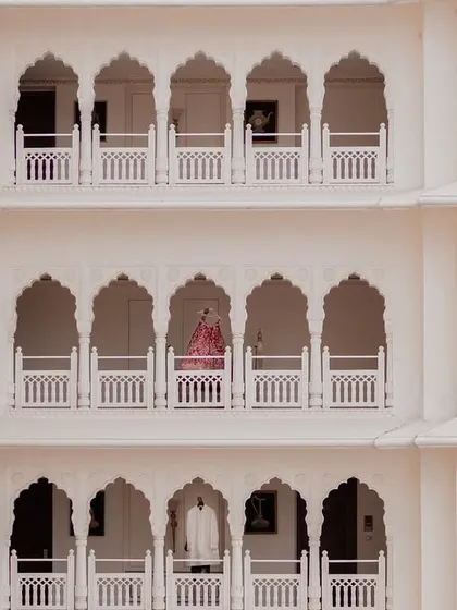 A breathtaking wide shot showing the bride and groom on separate balconies of a palace, a visual metaphor for two lives about to join. This architectural portrait highlights the grandeur of a destination wedding venue.