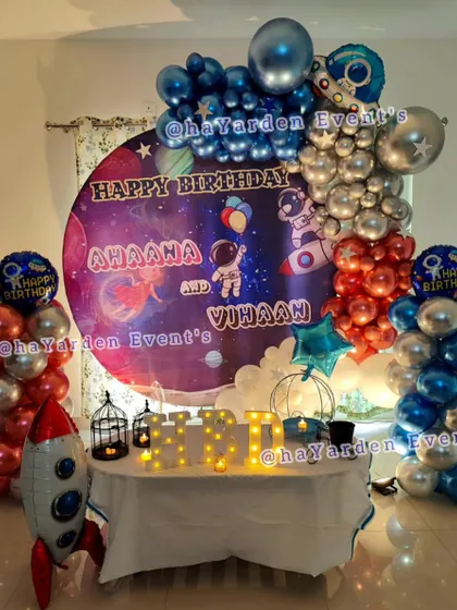 A complete space-themed birthday setup with a large galaxy backdrop, rocket ship foil balloons, and balloon pillars.