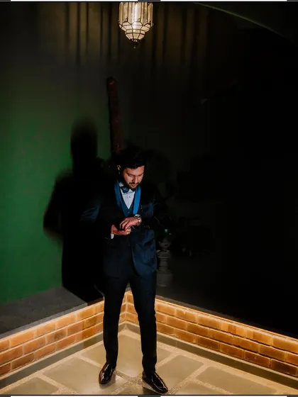 A full-length shot of the groom checking his watch, captured with dramatic lighting.