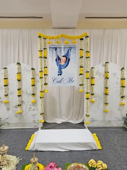 A wider perspective of the naming ceremony stage, showing how the elements fill the space. The white drapes provide a bright and clean canvas, making the yellow and white of the fresh flowers pop.