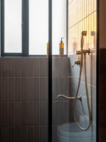 A close-up of the shower detail in a Calcutta bathroom. The combination of simple grey vertical tiles and antique brass fixtures creates a look that is understated, elegant, and timeless.