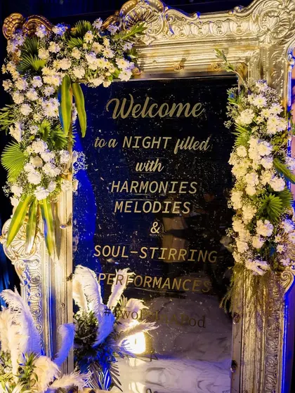 An opulent welcome sign on a silver-framed mirror, adorned with white flowers, perfect for a glamorous Sangeet or reception.