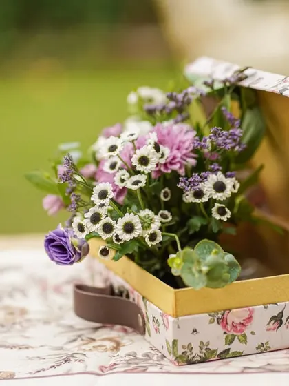 A small, floral-printed suitcase used as a container for a beautiful bouquet, a creative and charming decor detail.