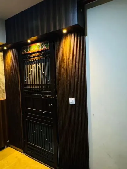 A close-up of a main door entrance we designed at Logix Blossom County. The dark wood paneling and warm spotlights create a sophisticated and inviting entryway.