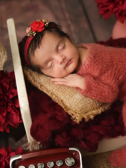 A side view of the newborn in her red-themed bed, showing her sweet sleeping profile.