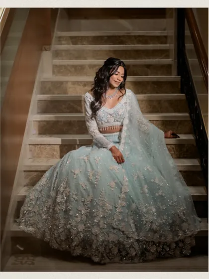 An elegant seated portrait of the bride on the stairs, her voluminous lehenga spread out around her. This classic pose creates a regal and timeless bridal image.