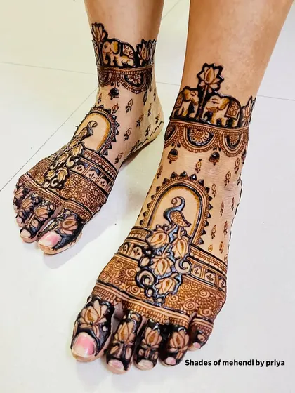 This foot mehendi design features peacocks in a jharokha, with delicate lotus and elephant details on the ankle band.