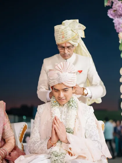A father adjusts his son's turban, a quiet moment of blessing and pride before the wedding ceremony begins.