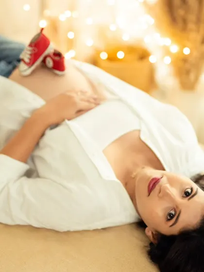 A creative shot of the mom-to-be lying down, with fairy lights in the background and tiny baby shoes on her bump.