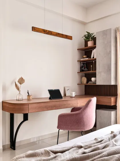 This elegant study nook features a floating wooden desk with a beautiful curved edge, supported by stylish black metal brackets. The combination of a pink upholstered chair and concrete-finish shelving creates a modern and sophisticated workspace.