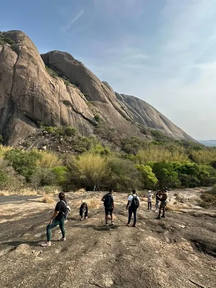 The crew spread out across a massive rock formation, with the peak of Savandurga in the background. The scale of the landscape is truly impressive.