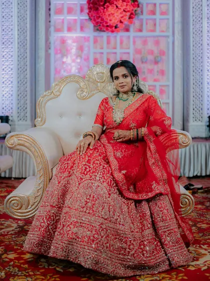 A stunning portrait of the bride in her red reception lehenga, seated elegantly on the stage.