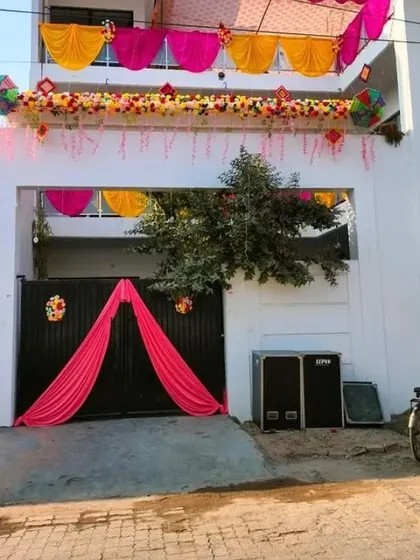 A house entrance decorated with a floral garland, hanging strings, and a pink drape over the gate.