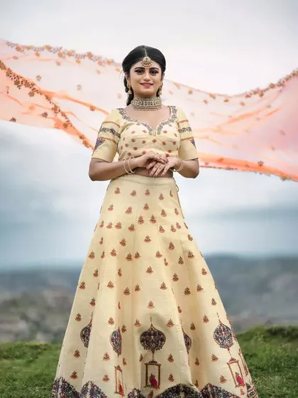 A beautiful cream-colored lehenga with delicate block-print style embroidery. The flowing dupatta adds a touch of drama for a pre-wedding photoshoot.