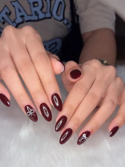 A moody coquette look with deep maroon polish and simple white bow accents.