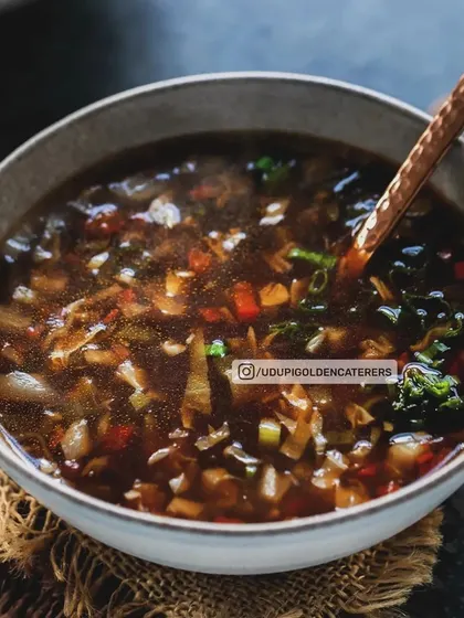 A bowl of our dark and flavorful vegetarian soup, possibly a Hot and Sour or Manchow variant, filled with finely chopped vegetables for a rich texture.