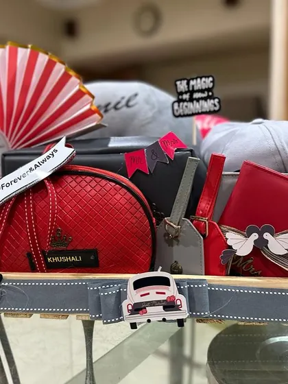 A vibrant red and grey themed hamper for a newlywed couple, celebrating "The Magic of New Beginnings". This gift includes personalized caps, matching pouches, and travel accessories for their journey ahead.