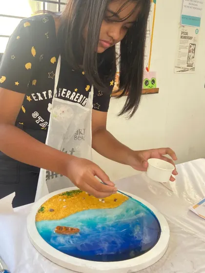 A student carefully places elements onto her resin beach art piece. This popular workshop teaches you how to create a beautiful ocean scene using resin, sand, and shells.