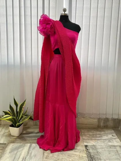 A modern take on the half saree, this hot pink outfit features a pleated skirt and a one-shoulder top with a dramatic organza flower detail.
