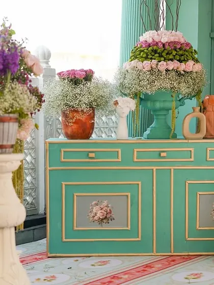 A wide view of a floral display area, with large arrangements on pedestals and a mint-green console table. The abundance of flowers creates a lush and romantic atmosphere.