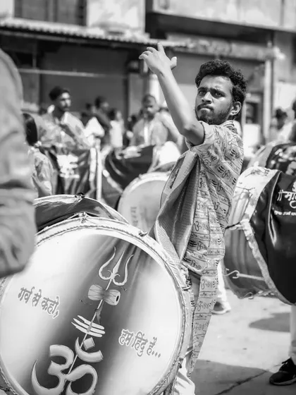 A black and white shot of a dhol player with an intense, focused expression.